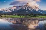 Picturesque landscape featuring a serene lake reflecting majestic mountains under a vibrant sunset sky.
