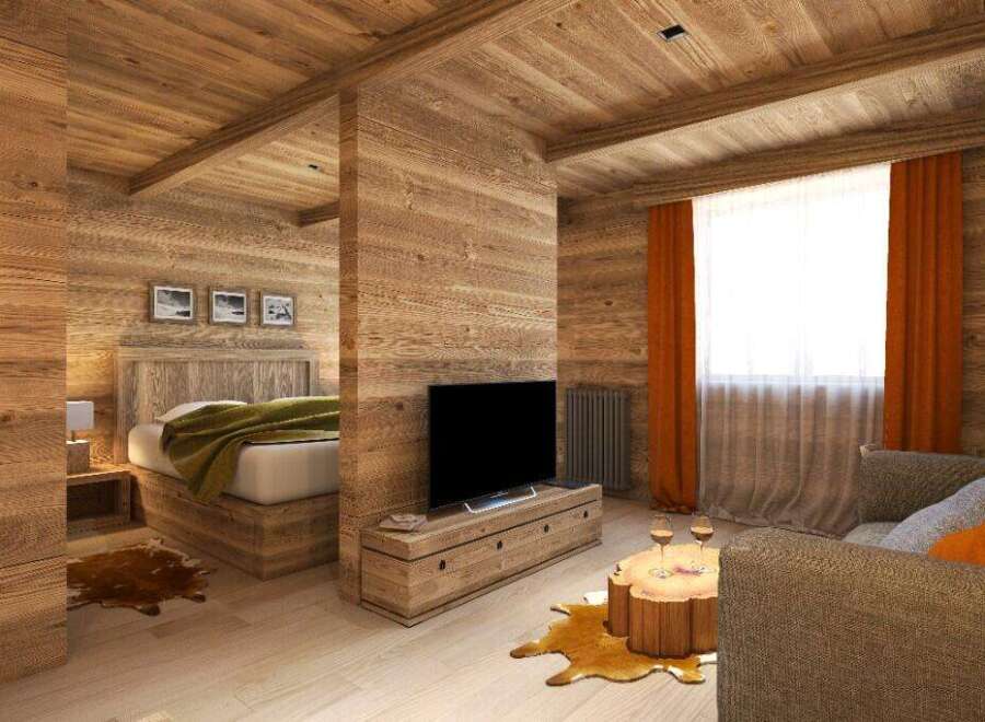 This stunning chalet-style room boasts a cozy living area with a rustic wooden coffee table and comfortable sofa, complemented by warm orange curtains and a large window.
