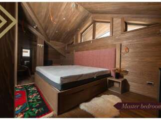 This master bedroom boasts a cozy and rustic atmosphere with wood paneling, a comfortable bed, and a unique rug.