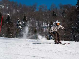 A skier cuts through fresh powder on a sunny winter day, leaving a trail of snow in their wake.