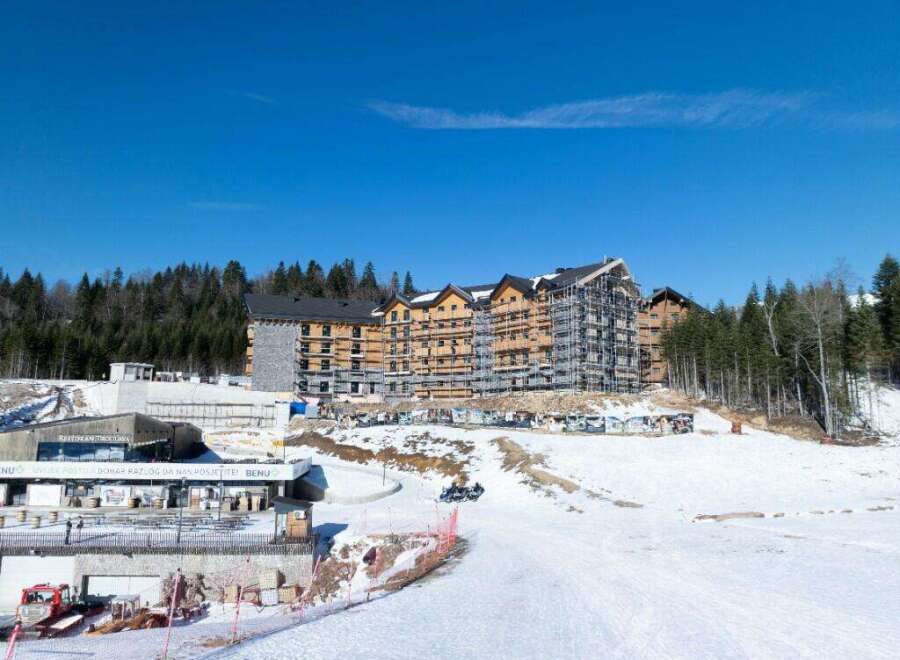This stunning ski resort boasts a modern hotel under construction, surrounded by breathtaking snowy landscapes and lush forests.