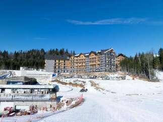 This stunning ski resort boasts a modern hotel under construction, surrounded by breathtaking snowy landscapes and lush forests.