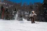 A skier cuts through fresh powder on a sunny winter day, leaving a trail of snow in their wake.