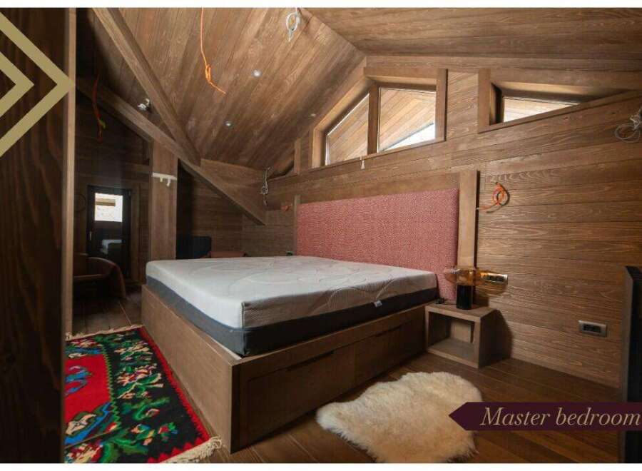This master bedroom boasts a cozy and rustic atmosphere with wood paneling, a comfortable bed, and a unique rug.