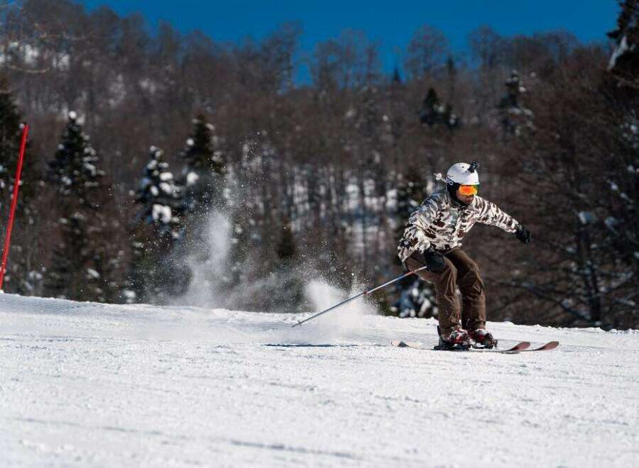A skier cuts through fresh powder on a sunny winter day, leaving a trail of snow in their wake.