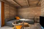 Cozy mountain chalet living room with wood-paneled walls and ceiling, featuring a comfortable gray sectional sofa and a rustic wooden coffee table.