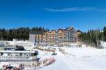 This stunning ski resort boasts a modern hotel under construction, surrounded by breathtaking snowy landscapes and lush forests.