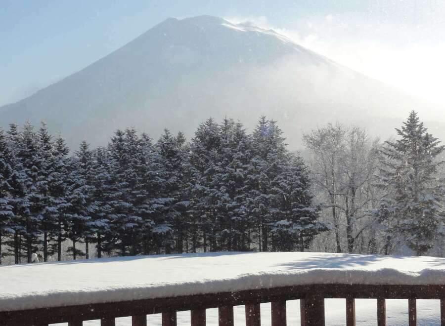 Snowy mountain view from a deck with a wooden railing.
