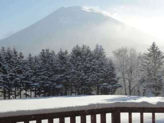 Snowy mountain view from a deck with a wooden railing.