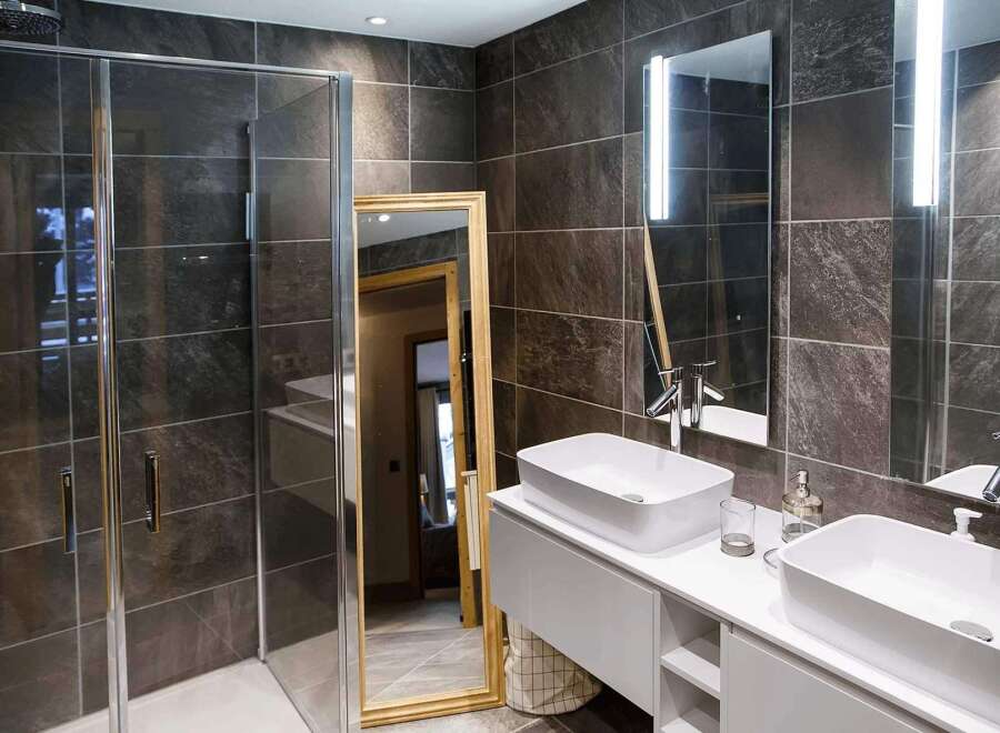 Luxurious bathroom with modern dark gray tiles, double sinks, and a spacious walk-in shower.