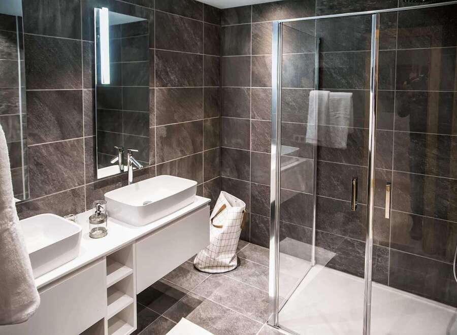 Modern bathroom with sleek dark tile, double vanity, and frameless glass shower enclosure.