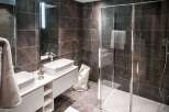 Modern bathroom with sleek dark tile, double vanity, and frameless glass shower enclosure.