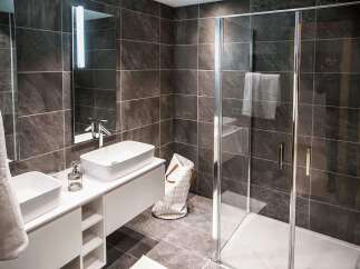 Modern bathroom with sleek dark tile, double vanity, and frameless glass shower enclosure.