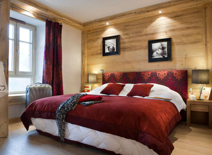 Cozy chalet bedroom with wooden walls, a plush red duvet, and tasteful decor.