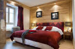 Cozy chalet bedroom with wooden walls, a plush red duvet, and tasteful decor.
