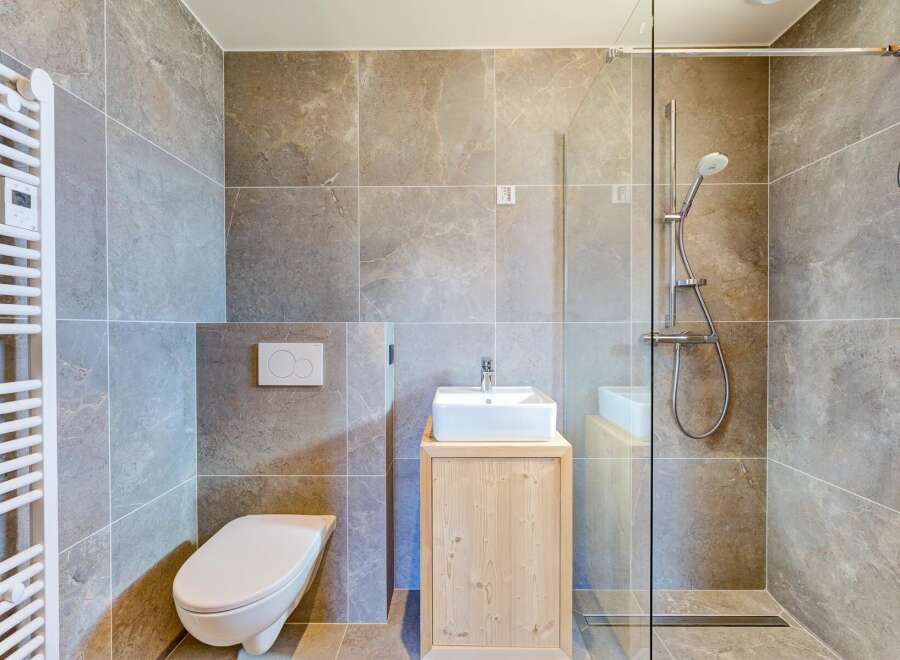 This modern bathroom features a sleek design with gray tile walls and a glass shower enclosure.