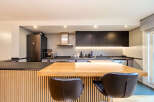 Modern kitchen with sleek dark cabinets, light gray backsplash, and a light wood island with bar stools.