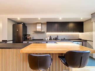 Modern kitchen with sleek dark cabinets, light gray backsplash, and a light wood island with bar stools.
