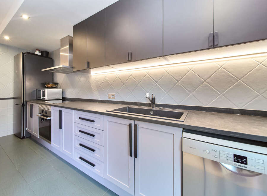 This stunning kitchen boasts sleek dark gray upper cabinets and light gray lower cabinets, complemented by modern black hardware.