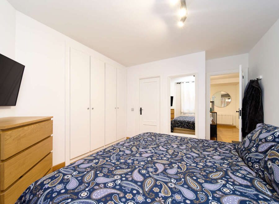 This cozy bedroom features a comfortable double bed with a paisley patterned duvet, built-in wardrobes offering ample storage, and a sleek modern TV.