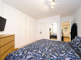 This cozy bedroom features a comfortable double bed with a paisley patterned duvet, built-in wardrobes offering ample storage, and a sleek modern TV.