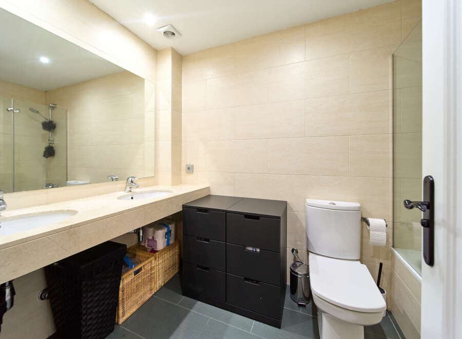 This stunning bathroom boasts modern double sinks, sleek dark cabinetry, and a stylish toilet.