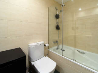 This modern bathroom boasts a sleek glass shower enclosure, a clean white toilet and bathtub, and stylish beige wall tiles.