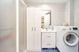 This stunning bathroom boasts a modern design with sleek white cabinetry, a spacious shower, and a convenient washer and dryer.
