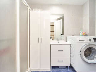 This stunning bathroom boasts a modern design with sleek white cabinetry, a spacious shower, and a convenient washer and dryer.