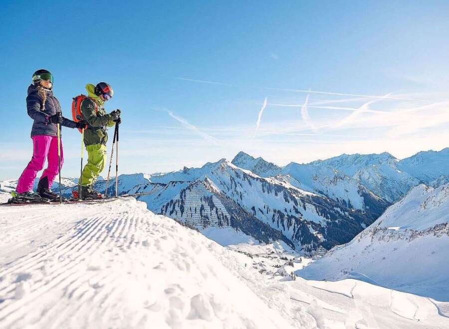 Skiers enjoy breathtaking panoramic views atop a snow-covered mountain, with pristine slopes and a stunning backdrop of snow-capped peaks.