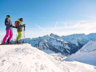 Skiers enjoy breathtaking panoramic views atop a snow-covered mountain, with pristine slopes and a stunning backdrop of snow-capped peaks.
