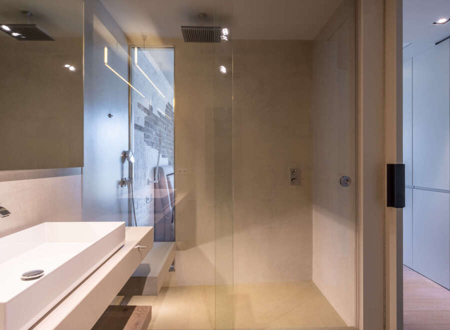 Modern bathroom with a glass shower enclosure, sleek sink, and exposed brick wall.