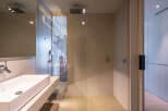 Modern bathroom with a glass shower enclosure, sleek sink, and exposed brick wall.