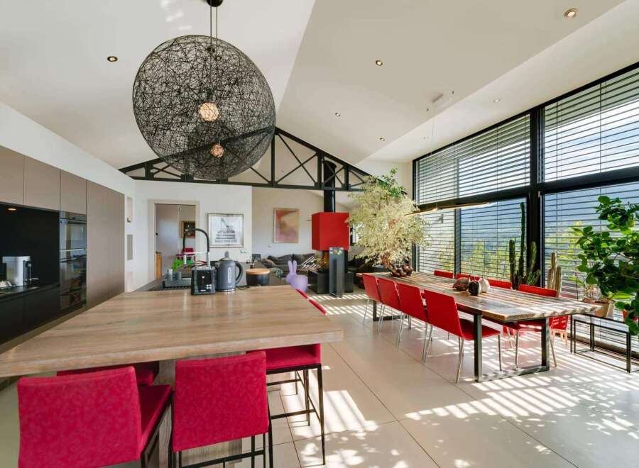 Stunning modern home boasts an open-concept kitchen and dining area with floor-to-ceiling windows offering breathtaking views.