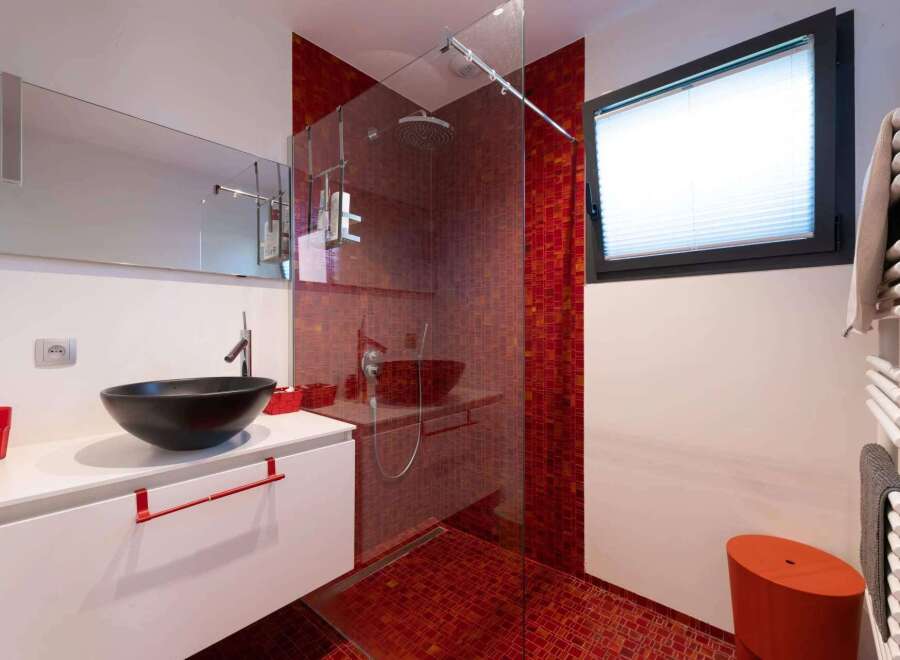 This stunning bathroom boasts a modern design with a sleek white vanity and a vibrant red mosaic tile shower.
