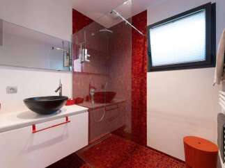 This stunning bathroom boasts a modern design with a sleek white vanity and a vibrant red mosaic tile shower.