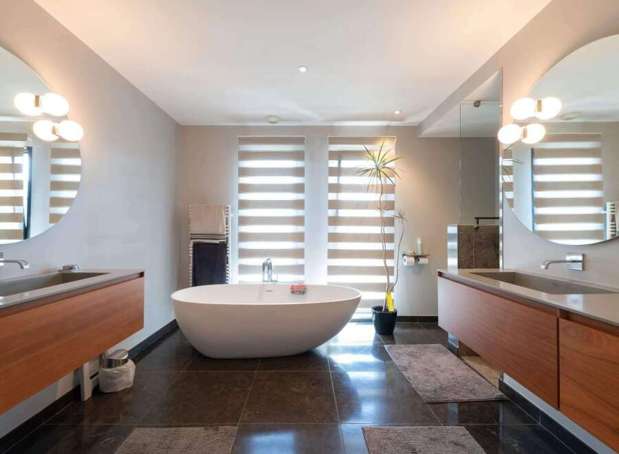 Luxurious bathroom with modern freestanding bathtub, double vanity with wooden cabinets, and large round mirrors.
