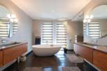 Luxurious bathroom with modern freestanding bathtub, double vanity with wooden cabinets, and large round mirrors.