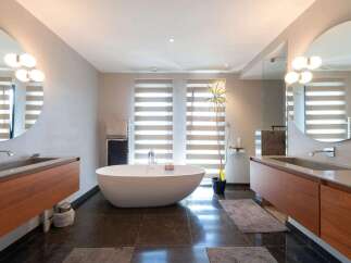 Luxurious bathroom with modern freestanding bathtub, double vanity with wooden cabinets, and large round mirrors.
