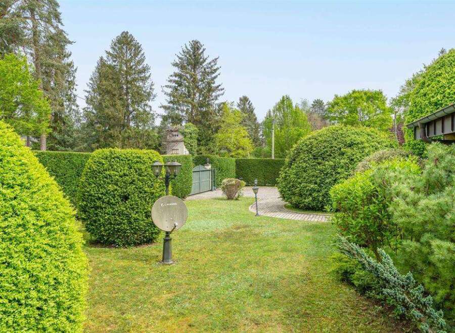 This stunning property boasts a meticulously landscaped garden, featuring lush green hedges, manicured lawns, and mature trees.