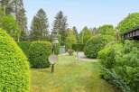 This stunning property boasts a meticulously landscaped garden, featuring lush green hedges, manicured lawns, and mature trees.