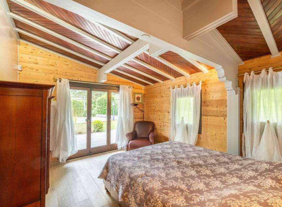 This stunning bedroom boasts a unique wooden ceiling and large windows overlooking a tranquil garden.