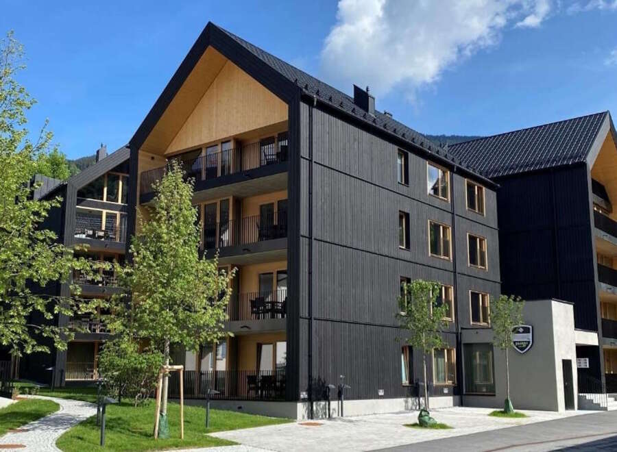 This stunning modern apartment building boasts a sleek black exterior with wood accents, offering breathtaking mountain views.