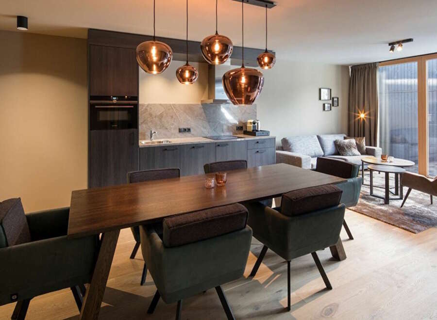 This modern apartment boasts an open-plan living area with a sleek kitchen, a dining table with comfortable seating, and a cozy living space featuring a large sofa and stylish armchairs.