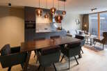 This modern apartment boasts an open-plan living area with a sleek kitchen, a dining table with comfortable seating, and a cozy living space featuring a large sofa and stylish armchairs.