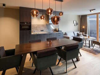 This modern apartment boasts an open-plan living area with a sleek kitchen, a dining table with comfortable seating, and a cozy living space featuring a large sofa and stylish armchairs.