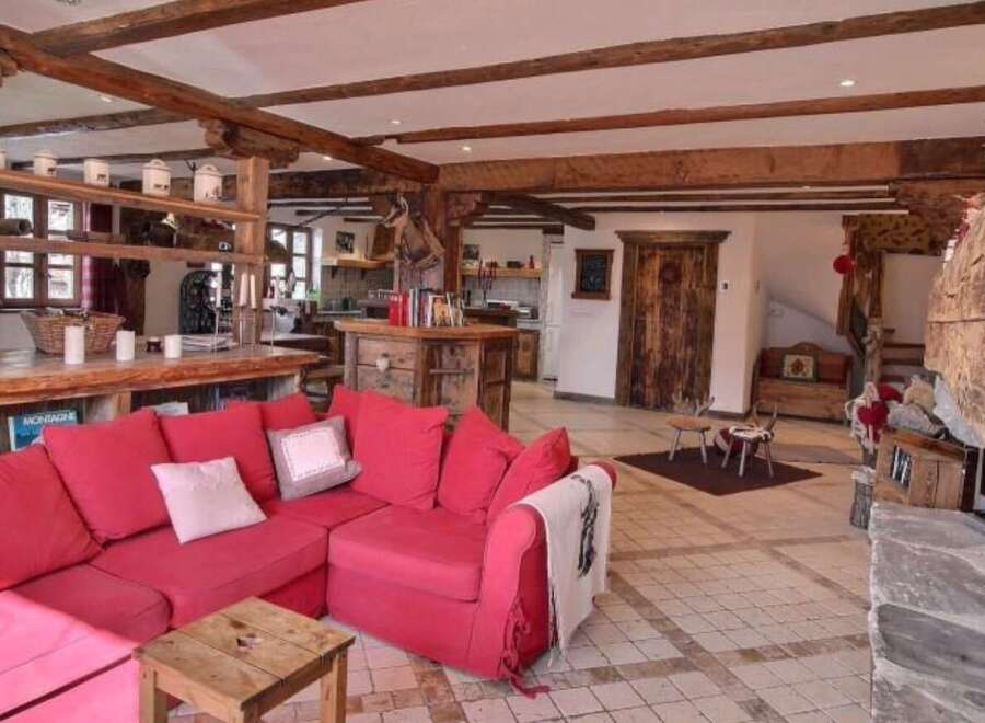 This stunning chalet boasts a spacious open-plan living area with exposed wooden beams, a cozy fireplace, and a large red sofa perfect for relaxing after a day on the slopes.