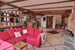 This stunning chalet boasts a spacious open-plan living area with exposed wooden beams, a cozy fireplace, and a large red sofa perfect for relaxing after a day on the slopes.