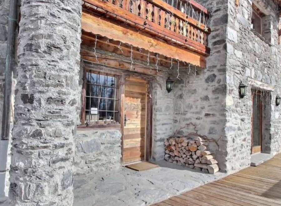 This stunning stone chalet boasts a charming wooden door and balcony, perfect for enjoying mountain views.