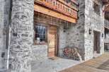 This stunning stone chalet boasts a charming wooden door and balcony, perfect for enjoying mountain views.